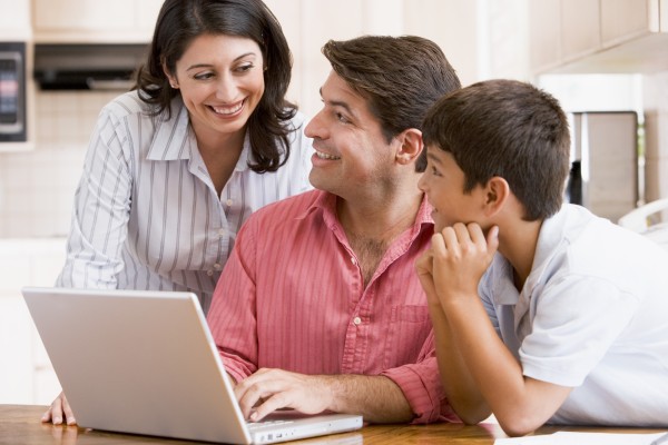 family in kitchen with laptop smiling