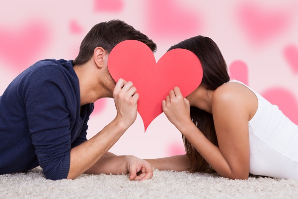 couple kissing behind heart while lying