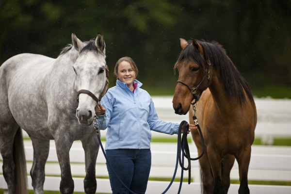 smiling young woman leading two horses