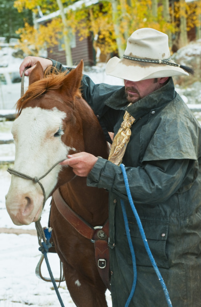 man putting bridle on horse