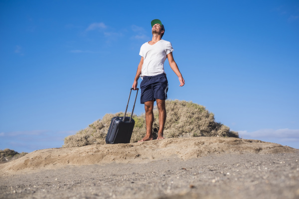 man standing with rolling suitcase at
