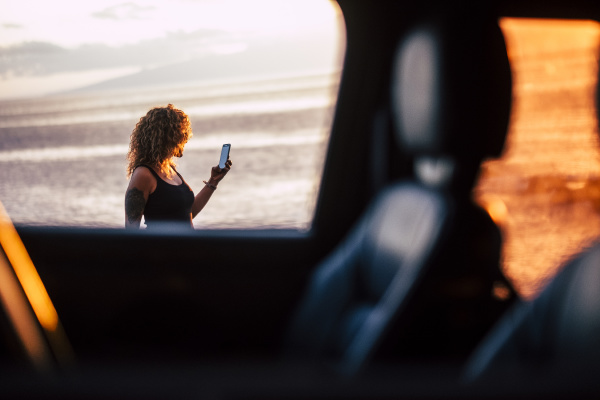 woman using smart phone behind car