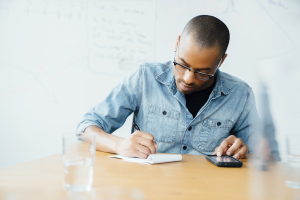 man using smart phone while writing