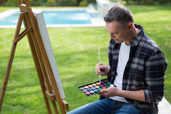 man painting on canvas in garden