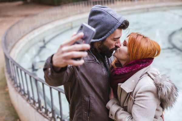 kissing couple taking selfie with smartphone