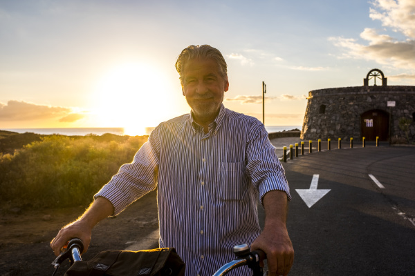senior man on bicycle at sunset
