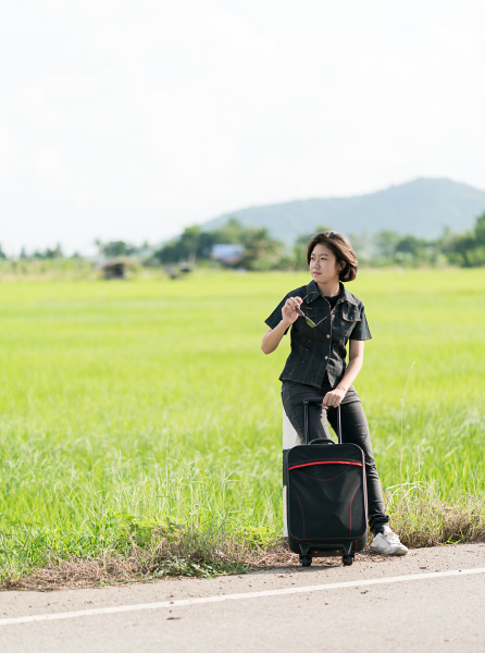 woman with luggage hitchhiking along a