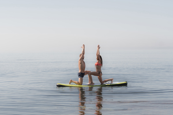 couple practicing yoga together on paddleboard