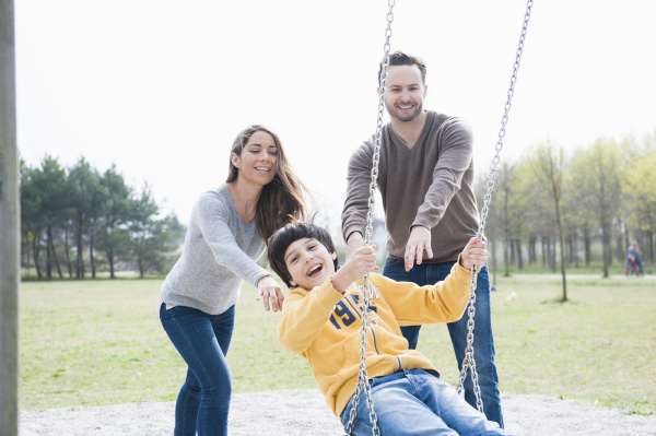 happy parents pushing son on swing