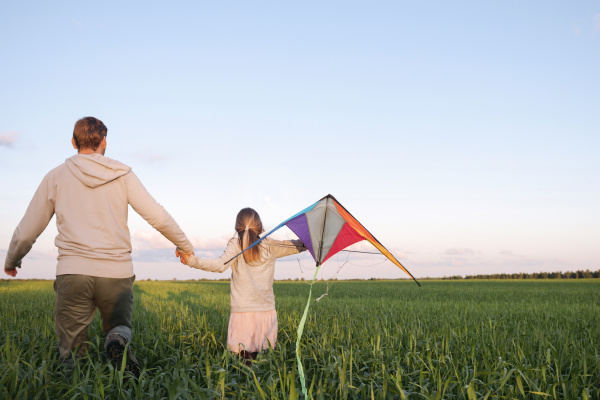 girl holding kite walking with father