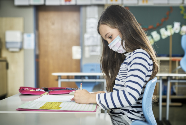girl wearing mask in classroom writing