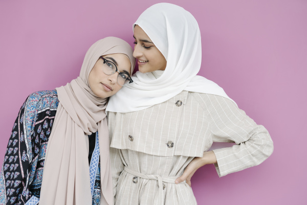 muslim sisters standing against purple background