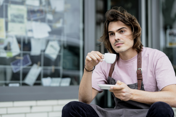 thoughtful male barista holding coffee sitting