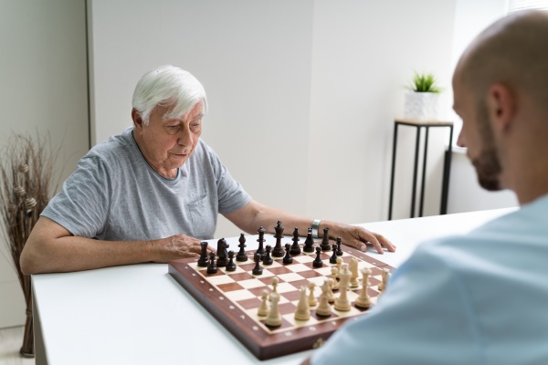 elderly senior playing chess with caregiver