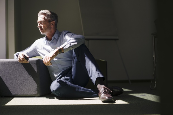 businessman sitting by hassock on floor