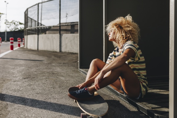 thoughtful woman sitting with skateboard while