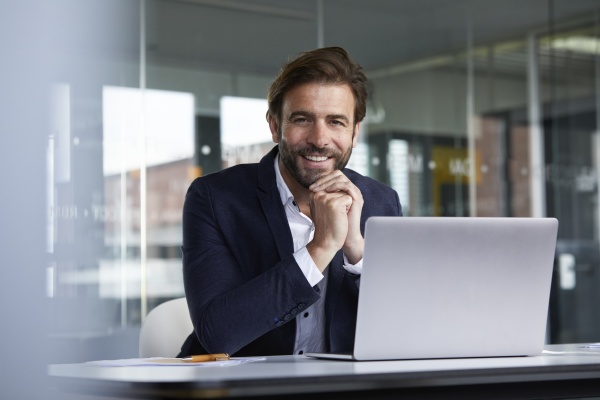 smiling businessman using laptop while sitting