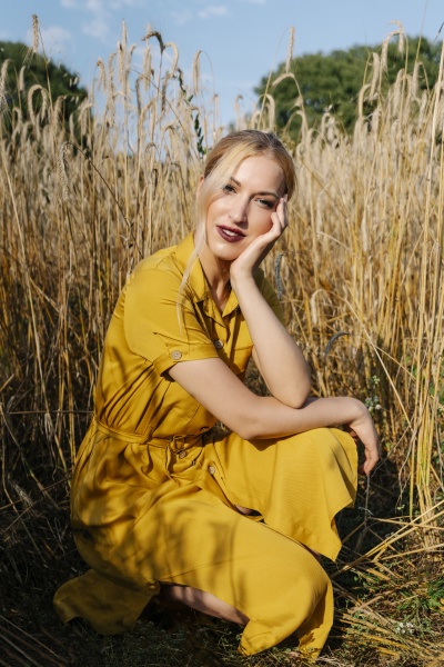 beautiful blond woman crouching against crops