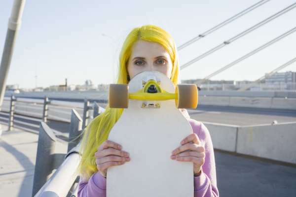 female hipster covering face with skateboard
