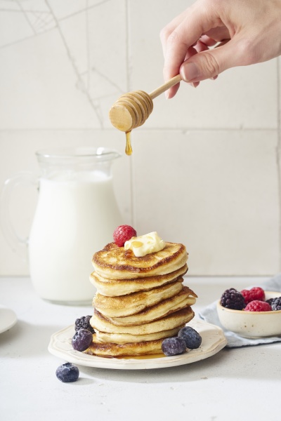 pouring honey pancakes with berries and