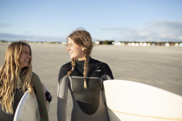 happy young female surfers carrying surfboards