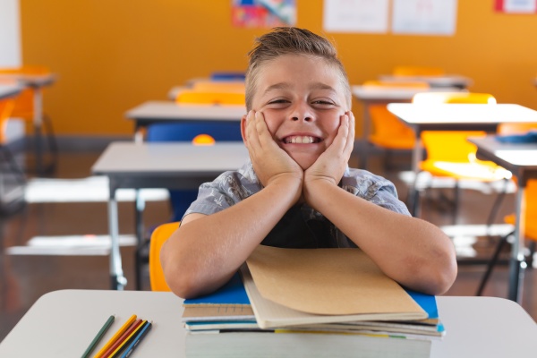 happy caucasian schoolboy sitting at desk
