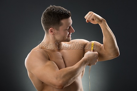 Muscular Asian man's arm flexing biceps with measuring tape Stock Photo