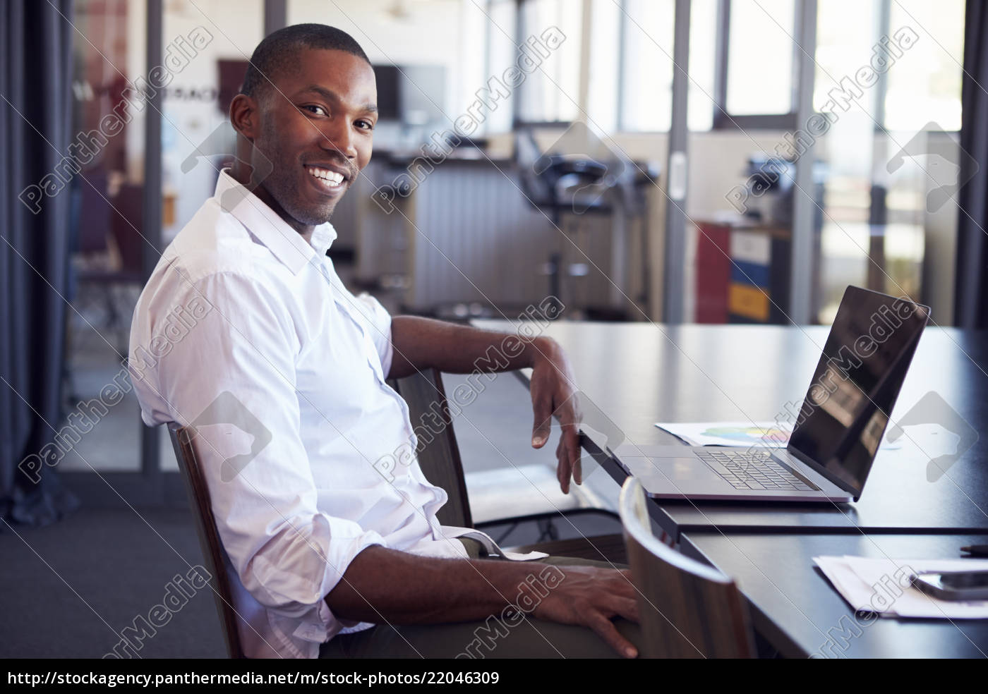Young Black Man Sitting At Desk In Office Smiling To Stock Photo