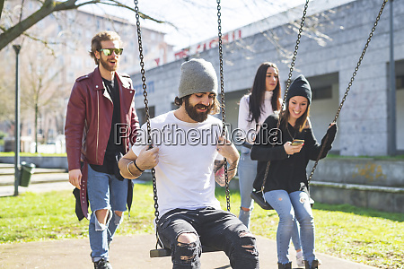 Man and woman pushing friends sitting on swings in - Royalty free photo ...